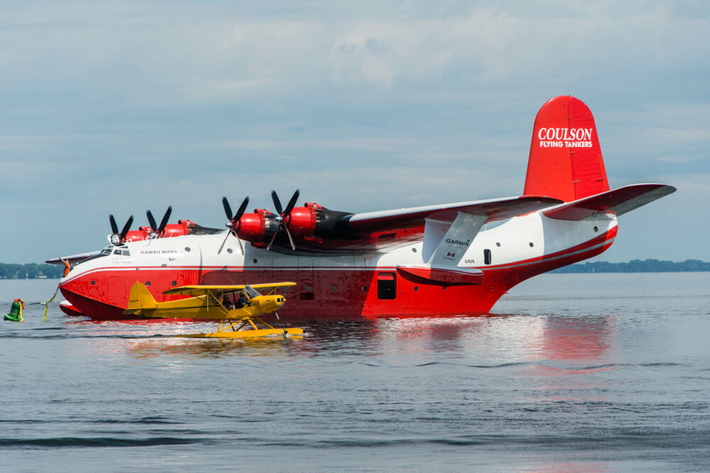 A Piper Cub floatplane passes in front of a Martin Mars flying boat