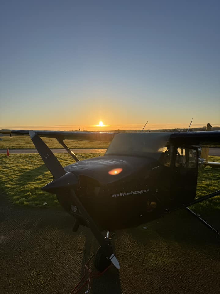 Light aircraft parked on grass in the sunrise.