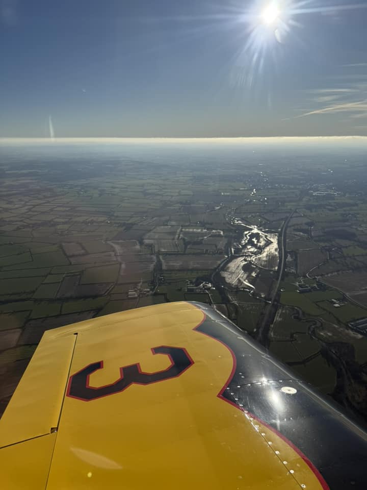 Aerial view of light aircraft wing with scenery in the background.