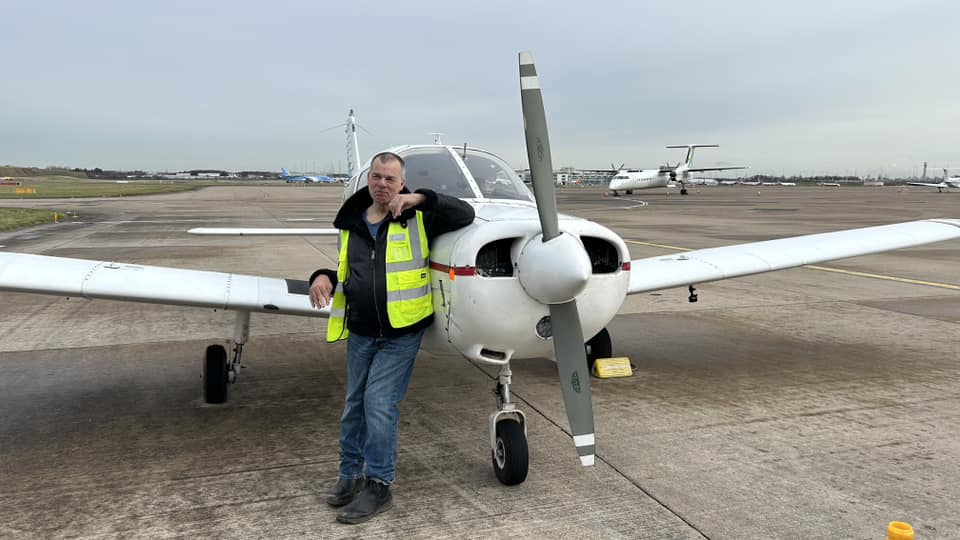 Man leaning against a light aircraft parked on the ground.