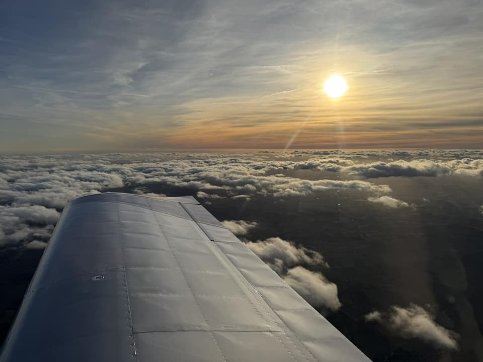 Aerial view of light aircraft wing above clouds, in the sunset.