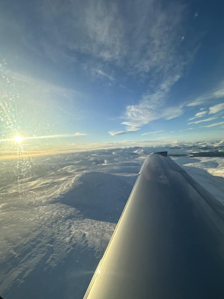 Light aircraft wing over snow-covered landscape.