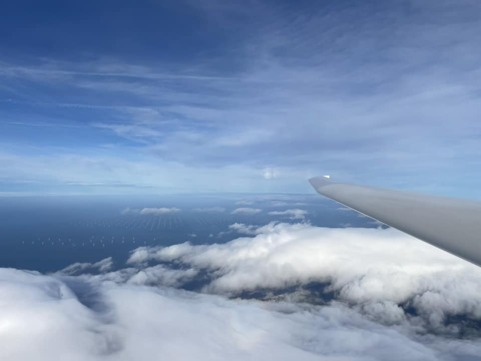 Glider wing with clouds below.