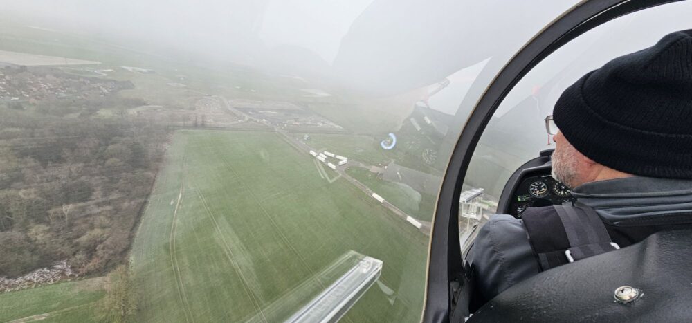 Light aircraft over grass runway.